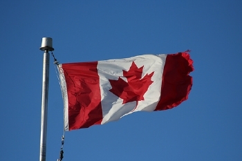 Canadian flag on a pole, fully unfurled against a clear blue sky