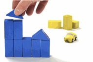 plain wooden blocks arranged in the shape of a building, a hand reaches in to place the final block to complete the building