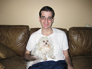 portrait of jason ross sitting on a couch holding a small, white, fluffy dog