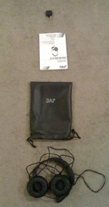 Arrangement by Charlie arranged vertically top to bottom: a black clip, a user manual for audio head phones, a pouch for holding the audio head phones, the audio head phones themselves