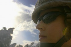 A woman in sunglasses and a Kevlar helmet looks off camera as the sun goes down in the background
