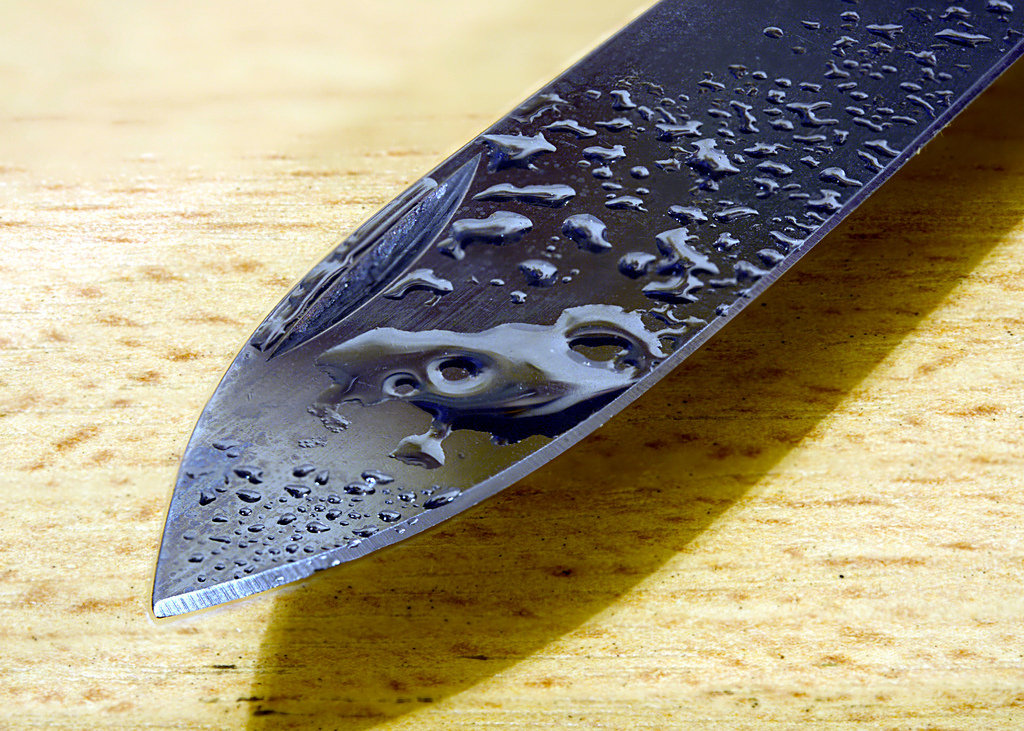 a knife's blade with droplets of water over a wood grain surface.