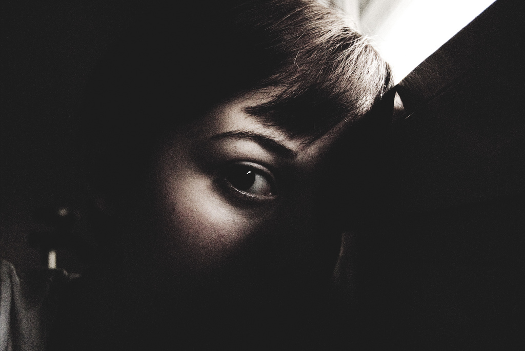 A dark image with a single shaft of light showing a woman's eye and brow.