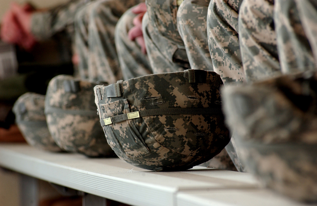 Army ACU helmets aligned in a row on a bench in front of a row of matching uniform parts.