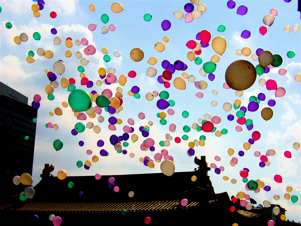 Hundreds of various coloured balloons fly free above the roof of a Buddhist temple.