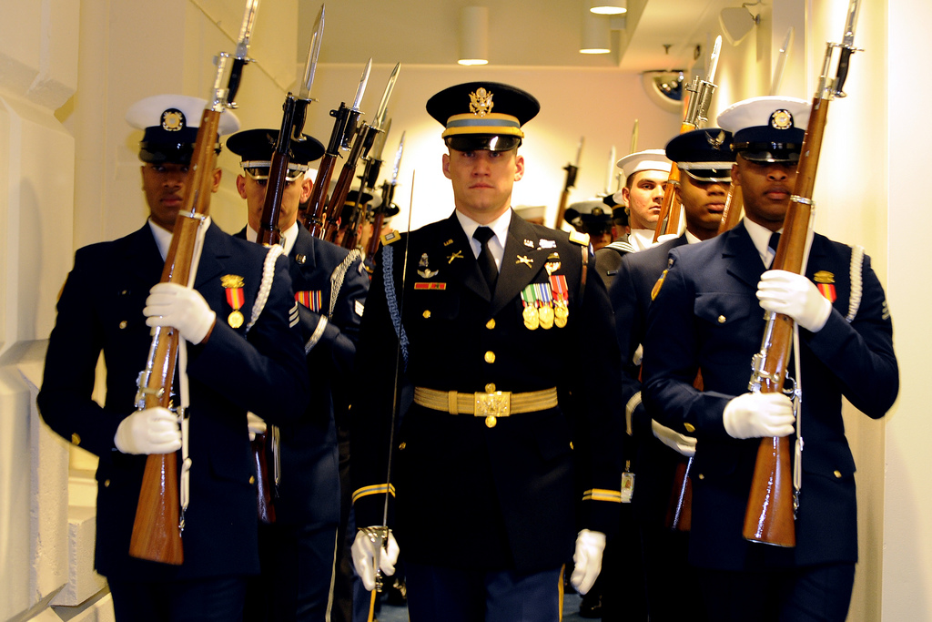 Several uniformed men carrying rifles standing in a tight hallway.