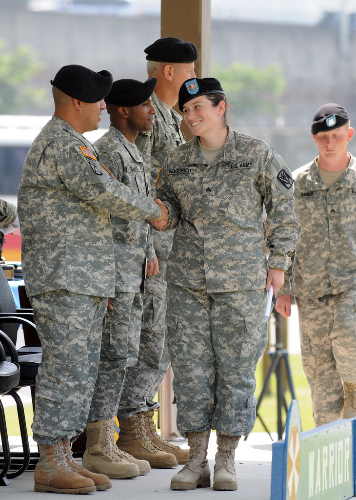 A woman in ACUs shakes hands with several men wearing the same.