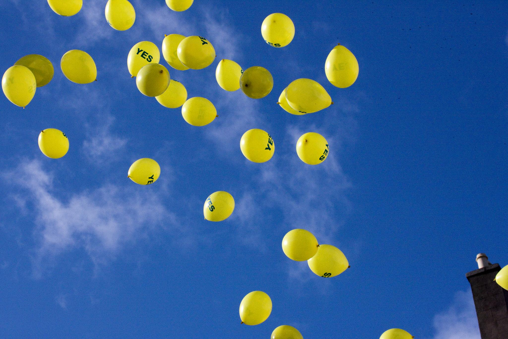A stark blue sky filled with bright yellow balloons that say the word 