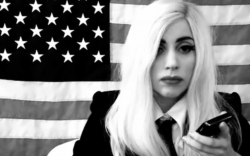 Screen shot of Lady Gaga. Black and white with a U.S. flag in the background.
